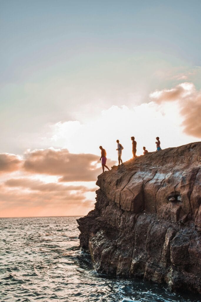 Group of people cliff jumping into the ocean at sunset. Captured in high detail.