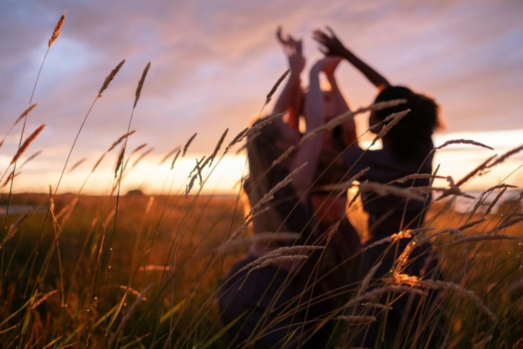Three women dance among tall grass at sunset, creating a serene and spiritual scene.