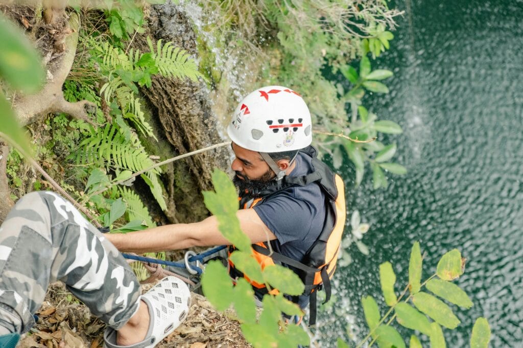 A man climbs a rock face near a waterfall, wearing a helmet and safety gear and practising mindful adventure.