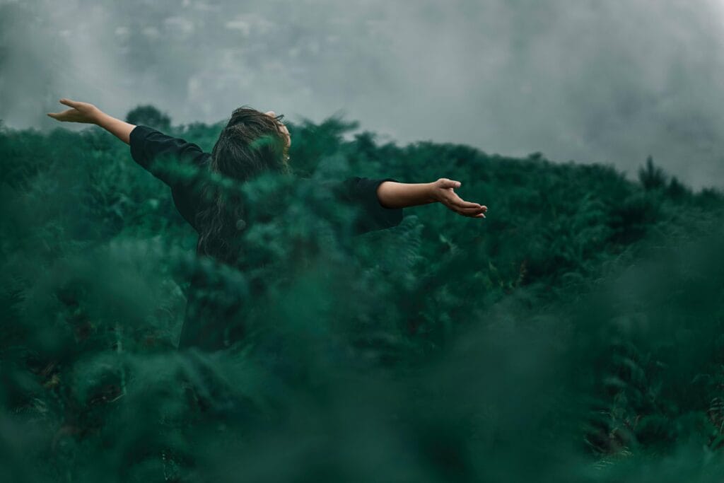 A woman with open arms enjoying  spiritual connection with nature for healing emotional pain.