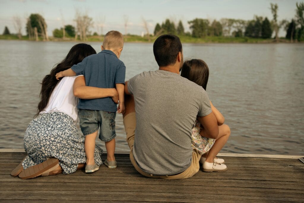 A family of four enjoys a peaceful moment sitting on a wooden deck by the river sustaining a sense of self while meeting the needs of children and spouse.