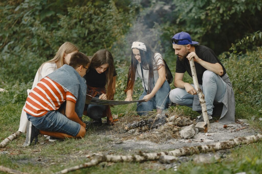 A diverse group of young adults gather around a campfire, exploring the benefits of outdoor education for student mental health
