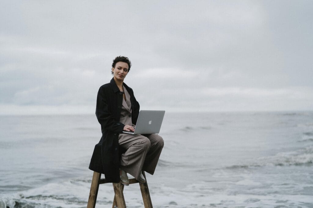 A person with a laptop sitting on a ladder by the ocean, symbolizing ambivert advantage.