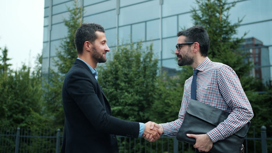 Two businessmen shaking hands outside an office building, symbolizing partnership.