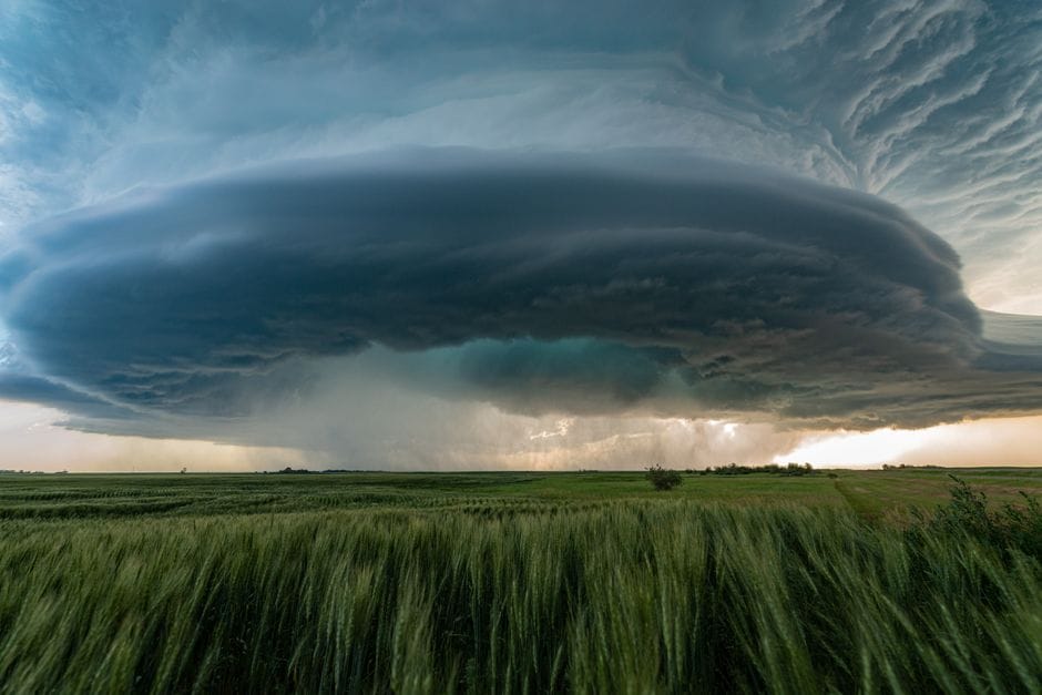 A powerful supercell storm looms over lush green fields showing what causes extreme weather changes,